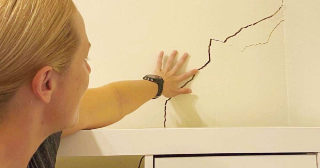 Homeowner pointing to a diagonal foundation settlement crack in an interior wall